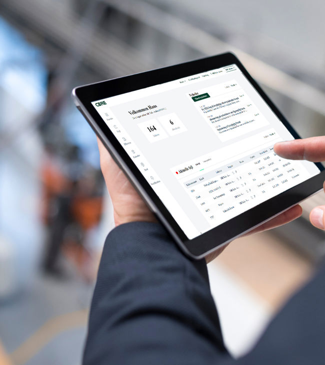 Mand bruger tablet med CBREs kundeportal, som giver overblik over kundens lovpligtige eftersyn