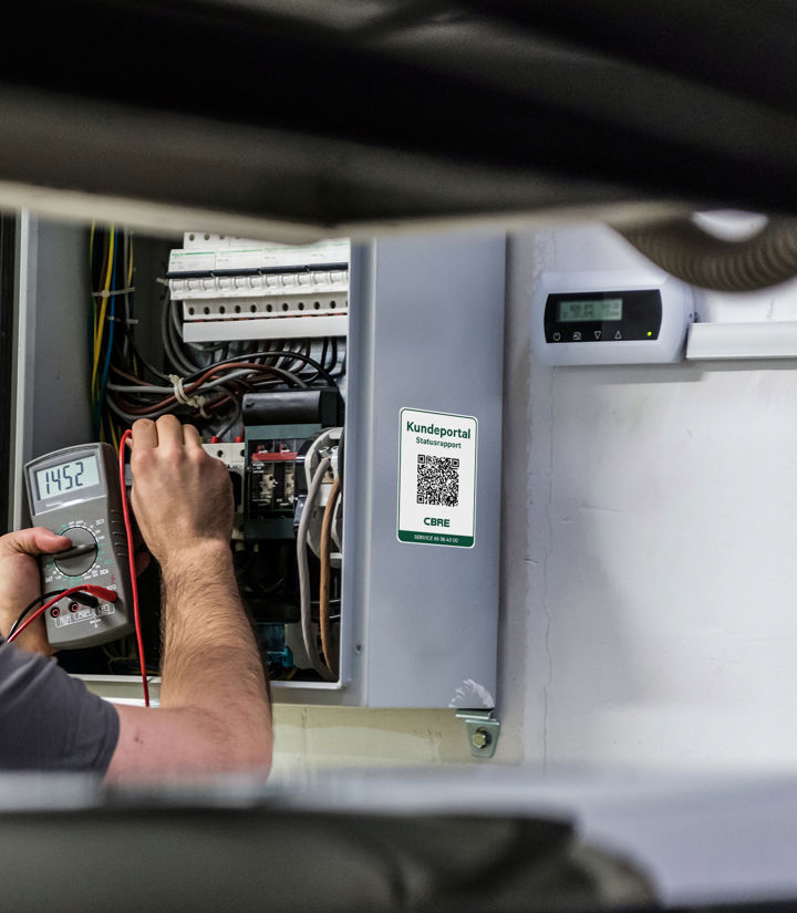 Tekniker udfører lovpligtigt eftersyn på tavle, hvor dokumentationen efterfølgende er tilgængelig i CBREs kundeportal via QR-koden